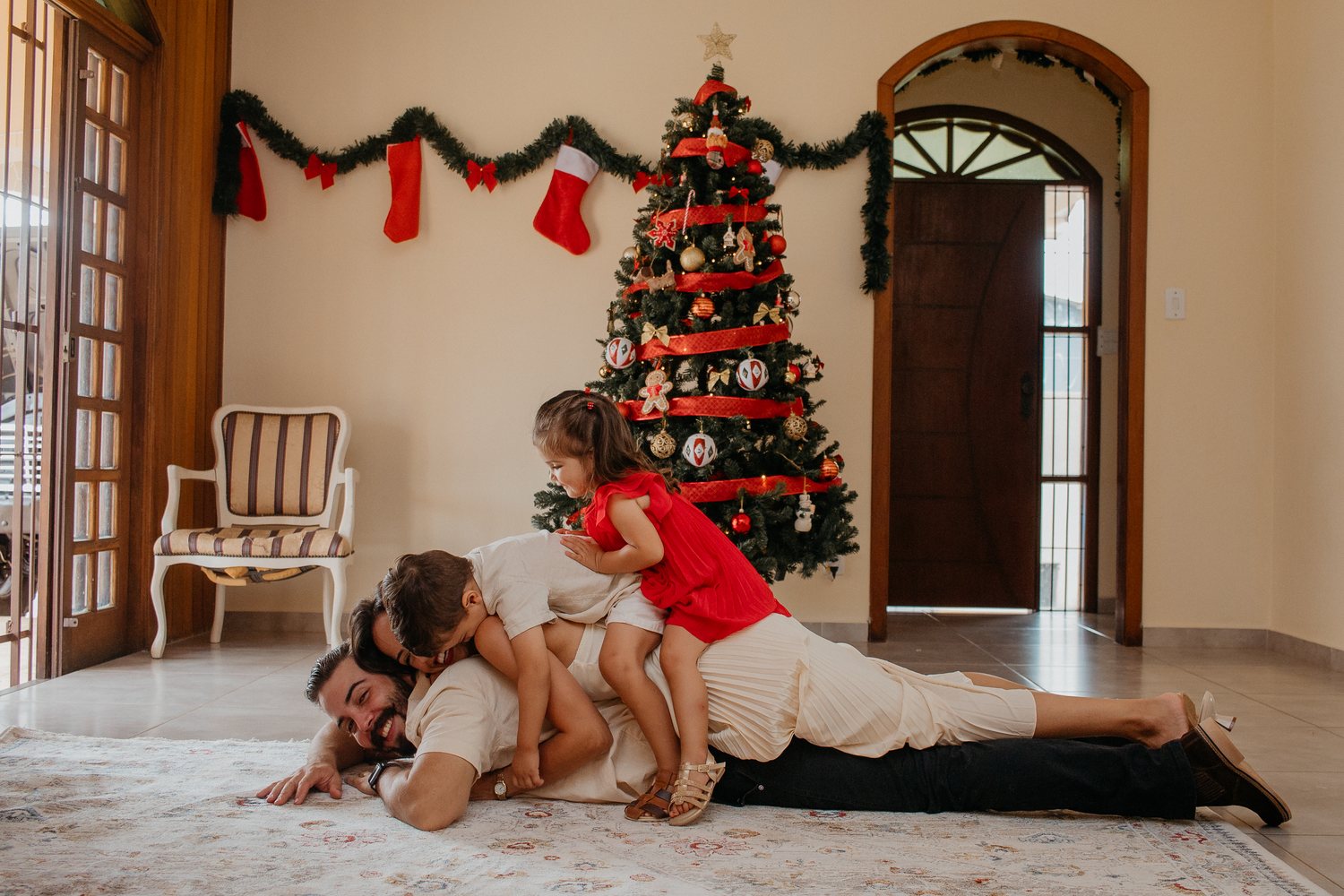 Minha família brincando no chão da sala da casa onde moramos hoje, ao lado da árvore de Natal